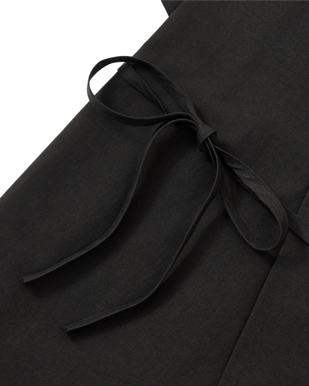 Close-up of the BLACK HANBOK LINEN SHIRT by Sundae School, showcasing a tied bow crafted from matching fabric straps, displayed flat against the black linen cotton material.
