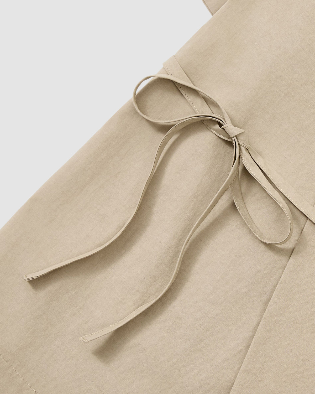 Close-up of the WHEAT HANBOK LINEN SHIRT by Sundae School, a beige cotton-linen blend with a side fabric waist tie bow, shown against a plain light background.