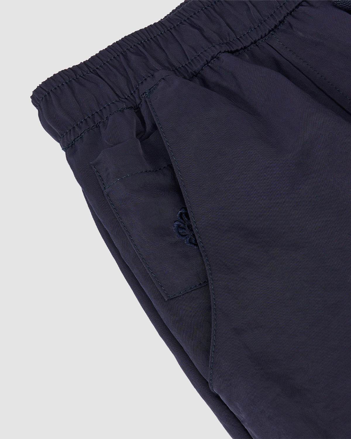 Close-up of Sundae School’s NAVY HANBOK BALLOON TRACK PANTS in navy nylon, featuring an elastic waistband, side pocket with detailed stitching, small embroidered logo near the pocket, and adjustable hems on a light grey background.