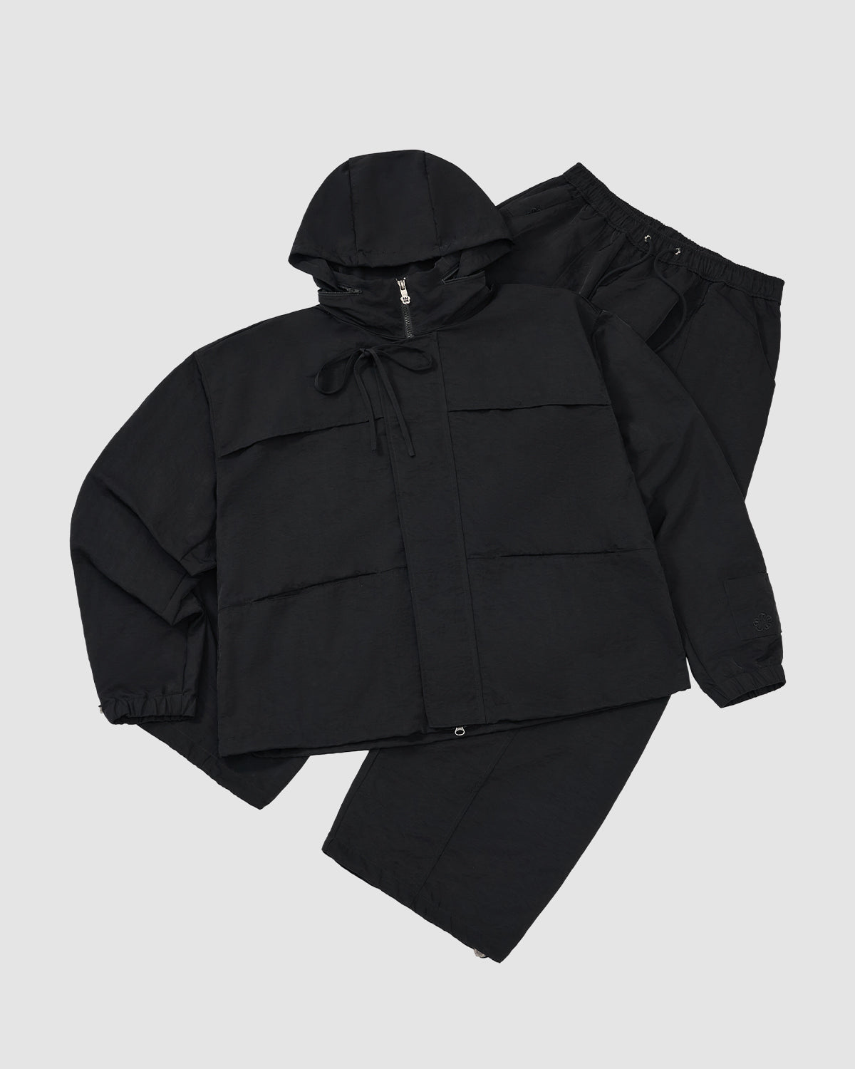 A flat lay of Sundae School's BLACK HANBOK BALLOON TRACK PANTS and a black hooded jacket with front pockets, both displayed on a light gray background.