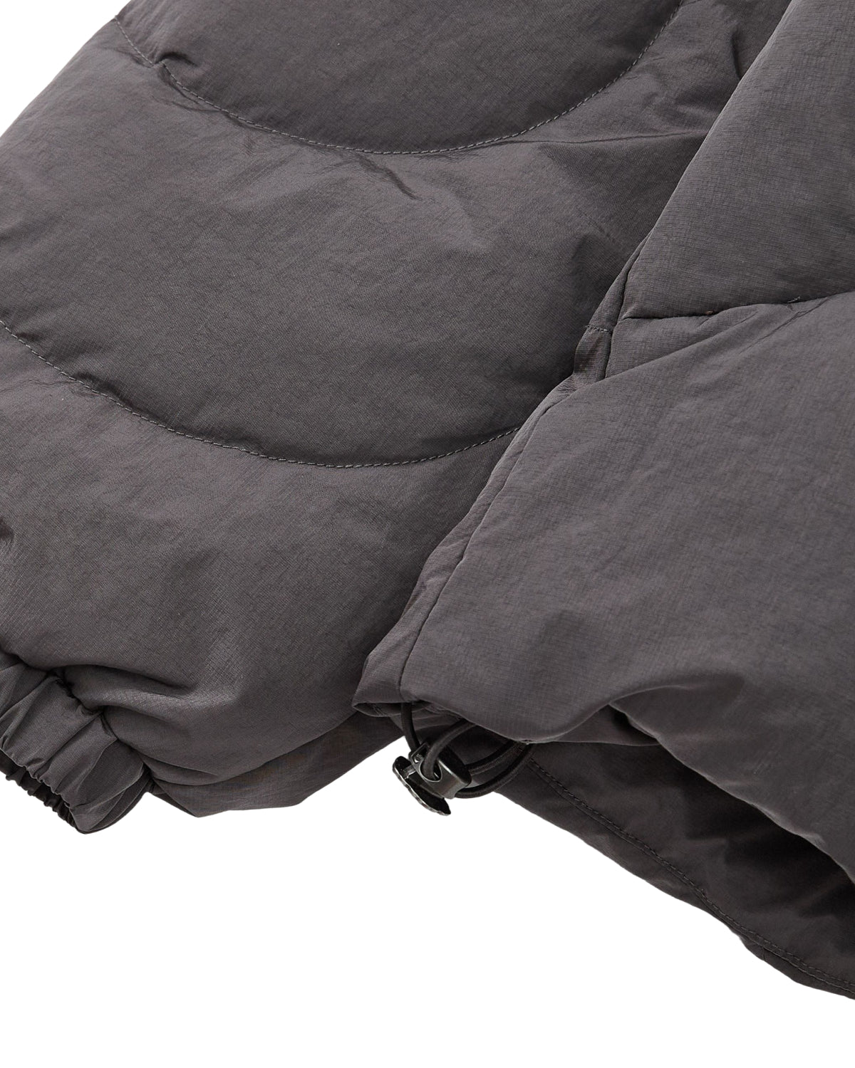 Close-up of the Sundae School CHARCOAL HEAVYWEIGHT MOCHI PUFFER, featuring a dark gray sleeve with an elasticated wrist and a drawstring cord at the hem for an adjustable fit.