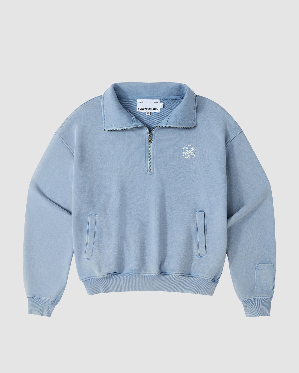The SKY BLUE HESTER QUARTER ZIP by Sundae School features a collar, front zipper, long sleeves, ribbed cuffs and hem, a small embroidered chest graphic, and an inner brand tag. Made from soft cotton sweat jersey for comfort.