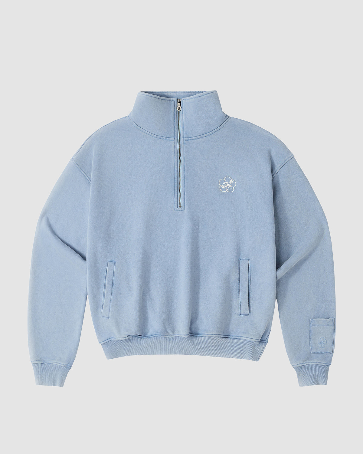 The Sundae School SKY BLUE HESTER QUARTER ZIP is an oversized sweatshirt with a high collar, long sleeves, front pockets, a flower logo on the left chest, and a sleeve pocket, shown against a plain background.
