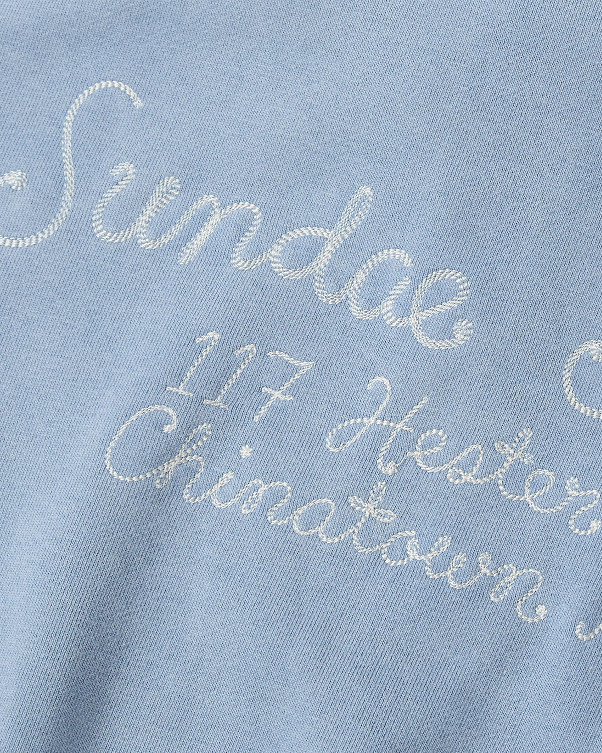 The SKY BLUE HESTER QUARTER ZIP by Sundae School is a light blue cotton pullover with white embroidered “Sundae,” “117 Hester,” and “Chinatown” text, featuring standout stitching and an oversized quarter zip for a modern look.