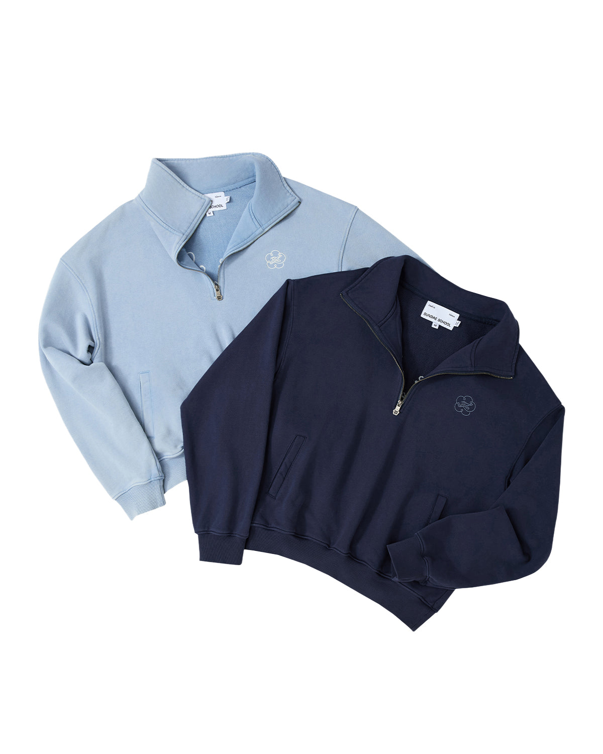 The SKY BLUE HESTER QUARTER ZIP from Sundae School and a navy pullover are laid flat, overlapping each other. Both vintage cotton pullovers feature a small embroidered logo on the chest and funnel neck collars with partially open zippers.
