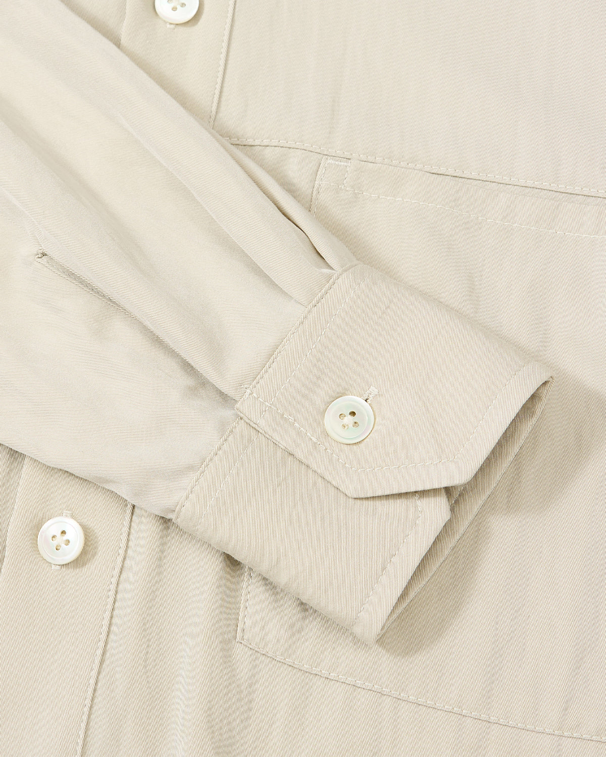 Close-up of the Sundae School IVORY HIGH NECK TIE SHIRT, highlighting its summer-weight fabric with subtle diagonal texture, a sleeve and cuff with white button, front buttons, and an oversized chest pocket seam.