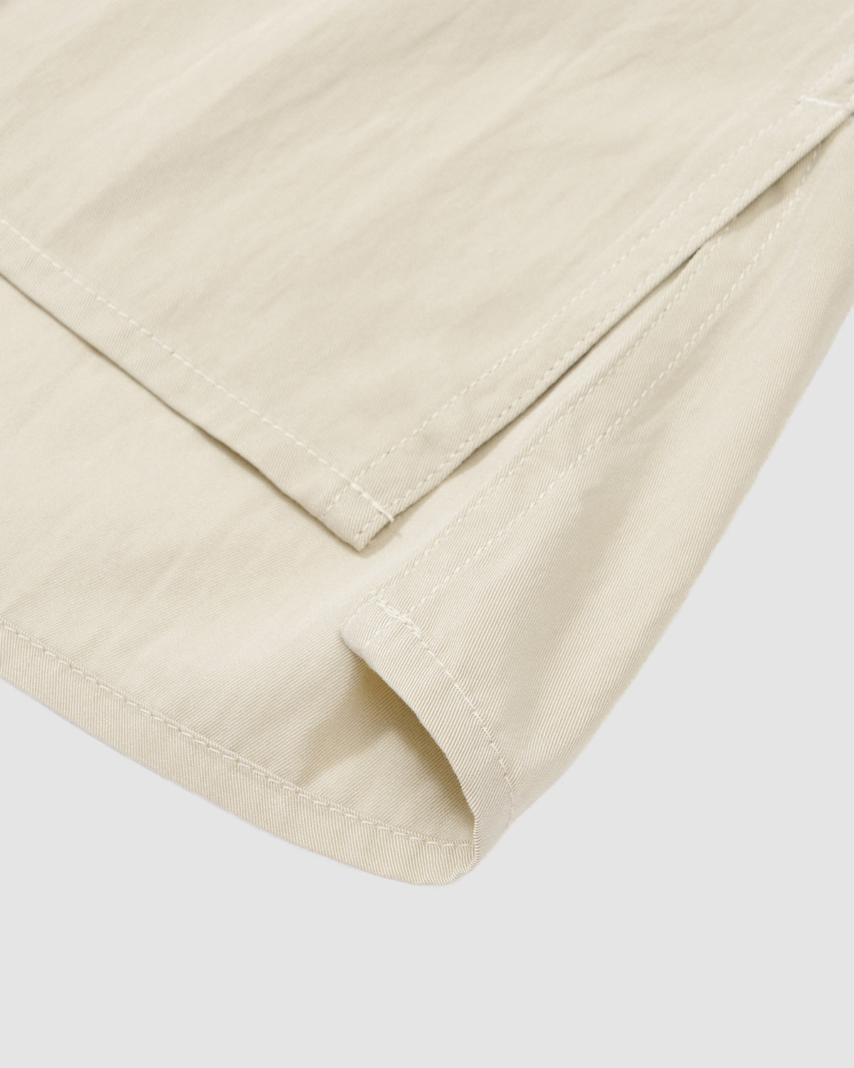 Close-up of the hem and side slit of the Sundae School IVORY HIGH NECK TIE SHIRT, highlighting stitching details and lightweight fabric texture on a light gray background.