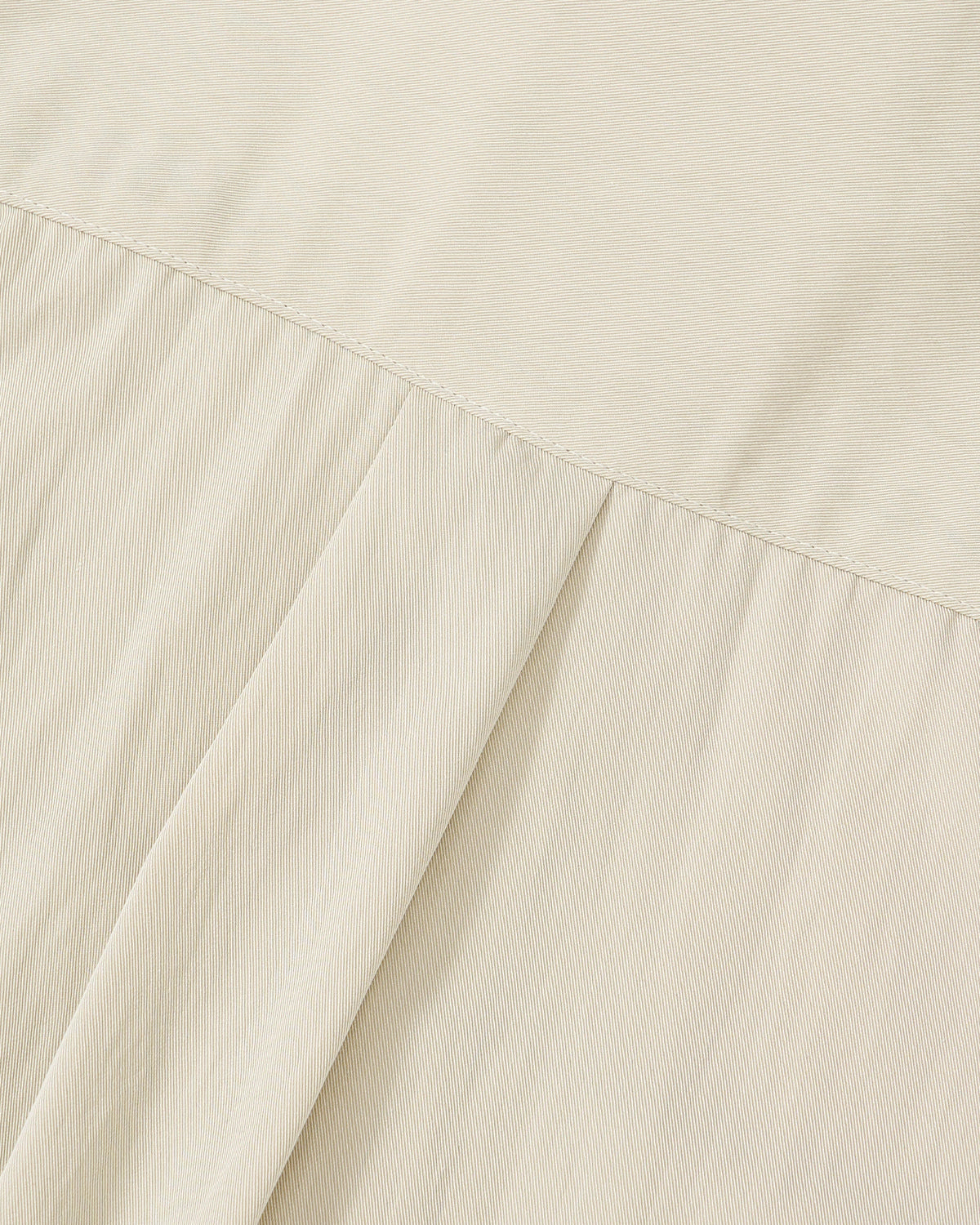 Close-up of the IVORY HIGH NECK TIE SHIRT by Sundae School shows light beige fabric with a diagonal seam; the smooth top contrasts with subtly striped, pleated folds below, highlighting its summer-weight design.