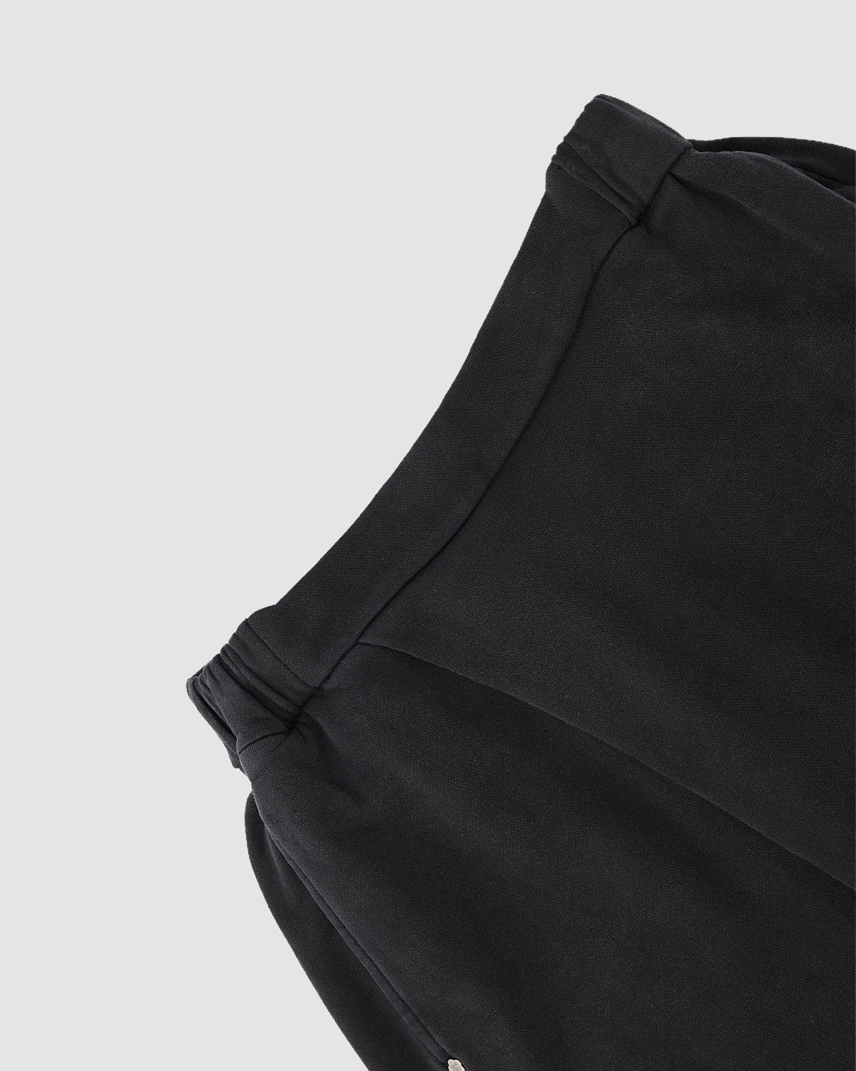 Close-up of the upper part of Sundae School's FADE BLACK WRAP SWEATBAJI, black cotton sweatpants with an elastic waistband, shown against a plain light grey background.