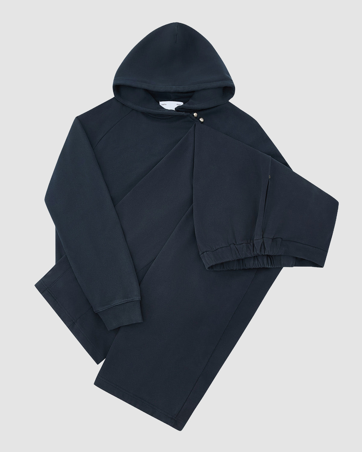 The INDIGO WASH WRAP SWEATBAJI by Sundae School, a dark navy blue cotton set with a drawstring hooded sweatshirt and matching sweatpants featuring an elastic waistband and cuffs, is laid flat on a light grey background.