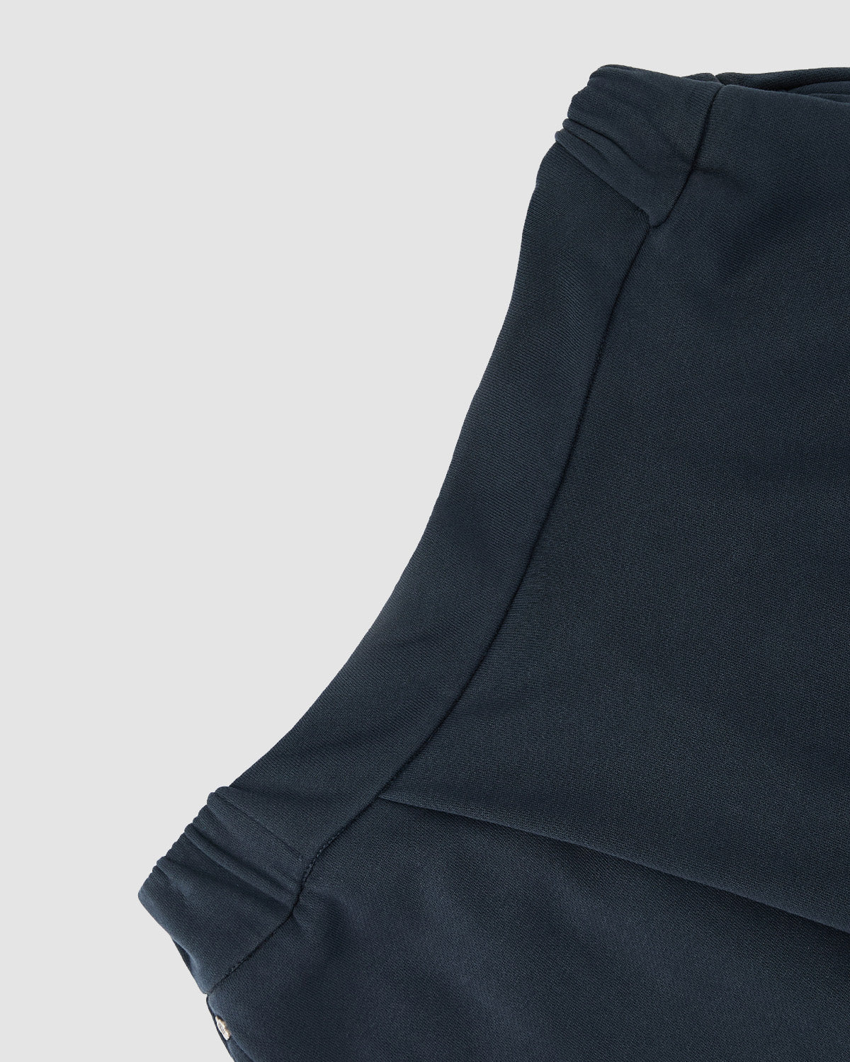 Close-up of the INDIGO WASH WRAP SWEATBAJI by Sundae School, highlighting the dark navy fabric texture and stitch detailing along the waistband and side seam against a light gray background.
