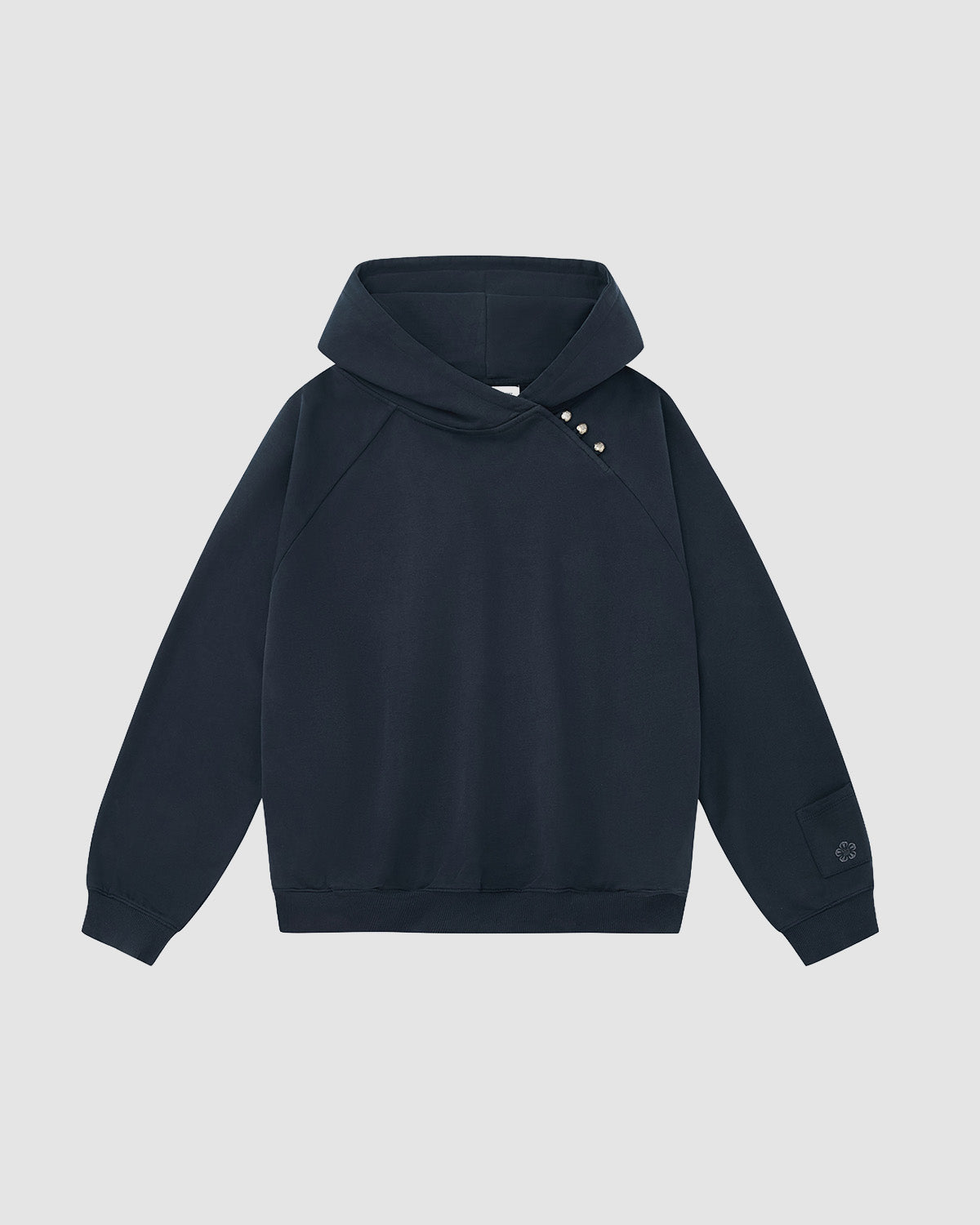 The INDIGO WASH HANBOK HOODIE by Sundae School is a black hoodie with an asymmetrical shoulder button, subtle flower-shaped design, and signature sleeve stash pocket, shown against a light gray background.