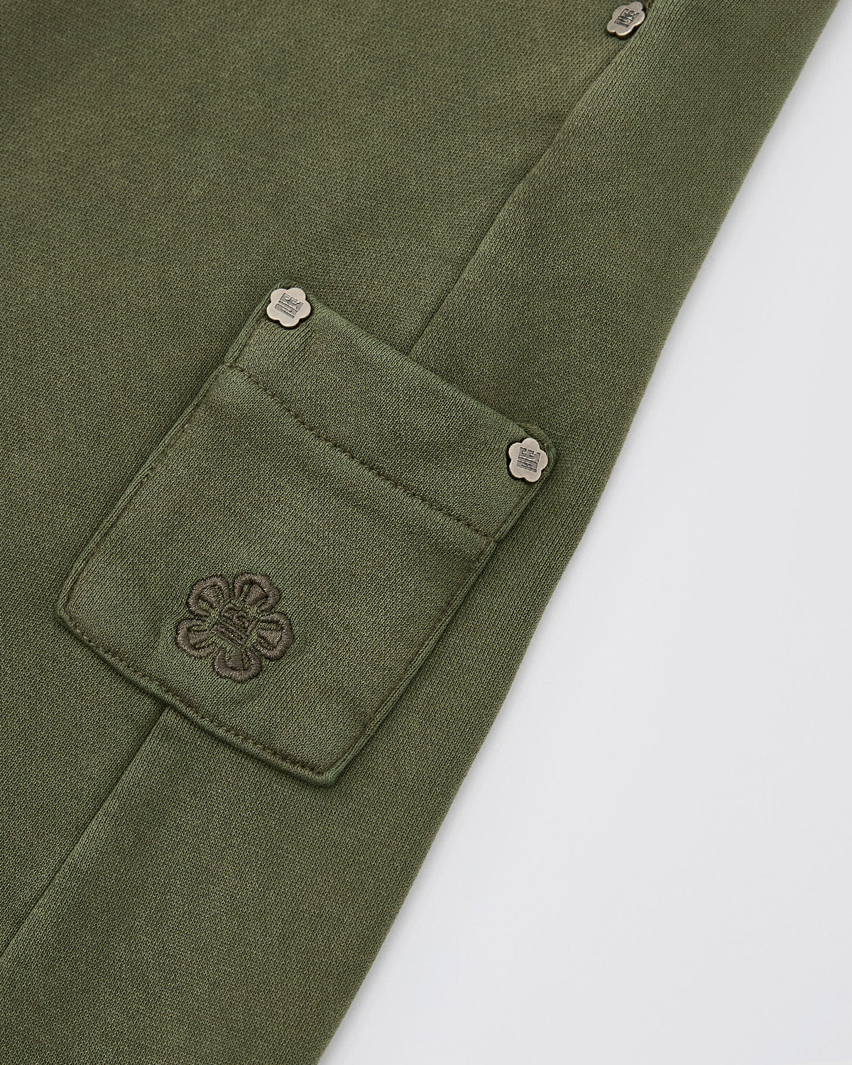 Close-up of Sundae School's KHAKI WRAP SWEATBAJI, featuring olive green fabric with a Hanbok-inspired small pocket, stitched flower design, and decorative metal rivets on the corners against a white background.