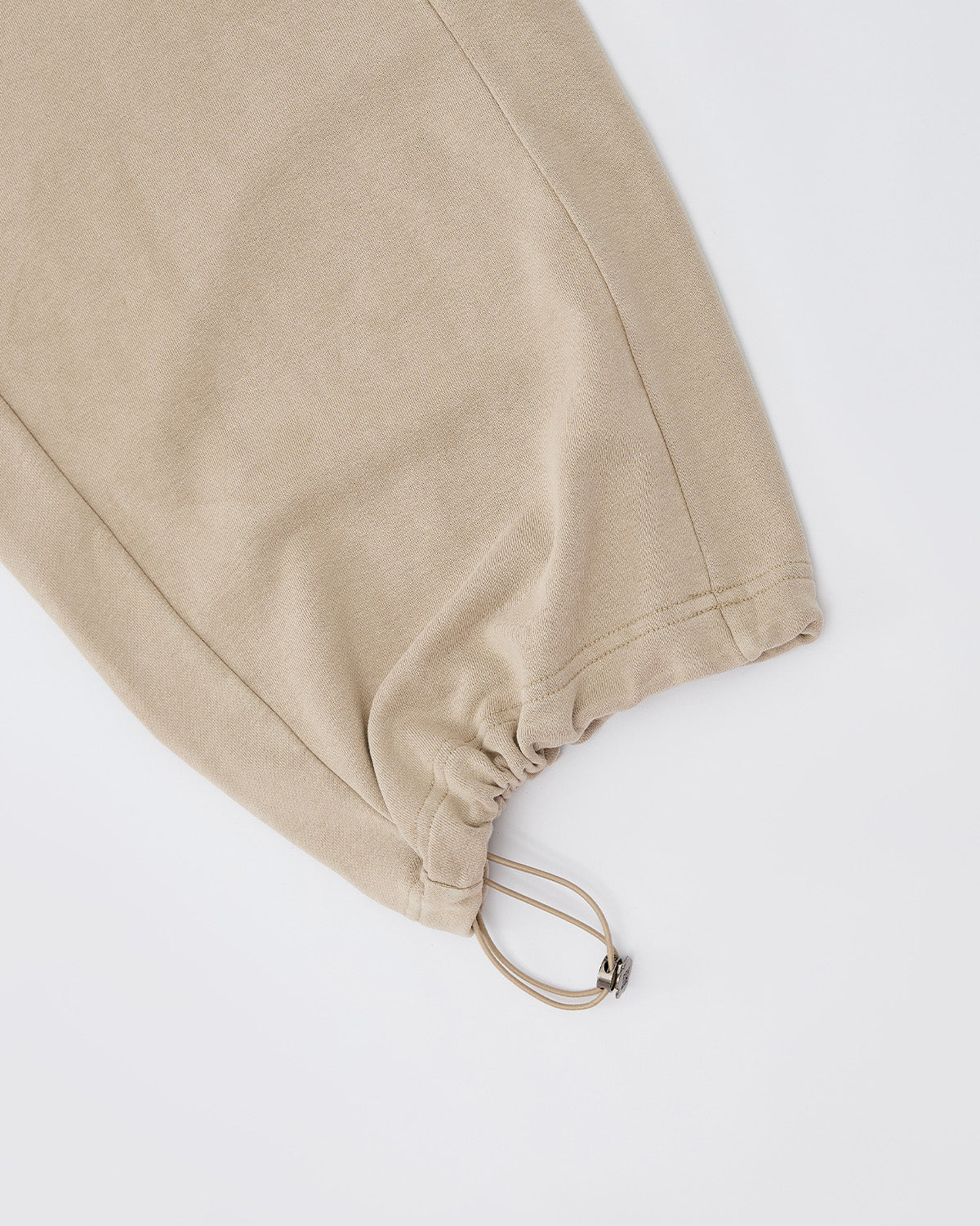 A close-up of the Sundae School TAUPE WRAP SWEATBAJI pant leg in beige 100% cotton, featuring an adjustable drawstring and toggle at the hem, set against a plain white background.
