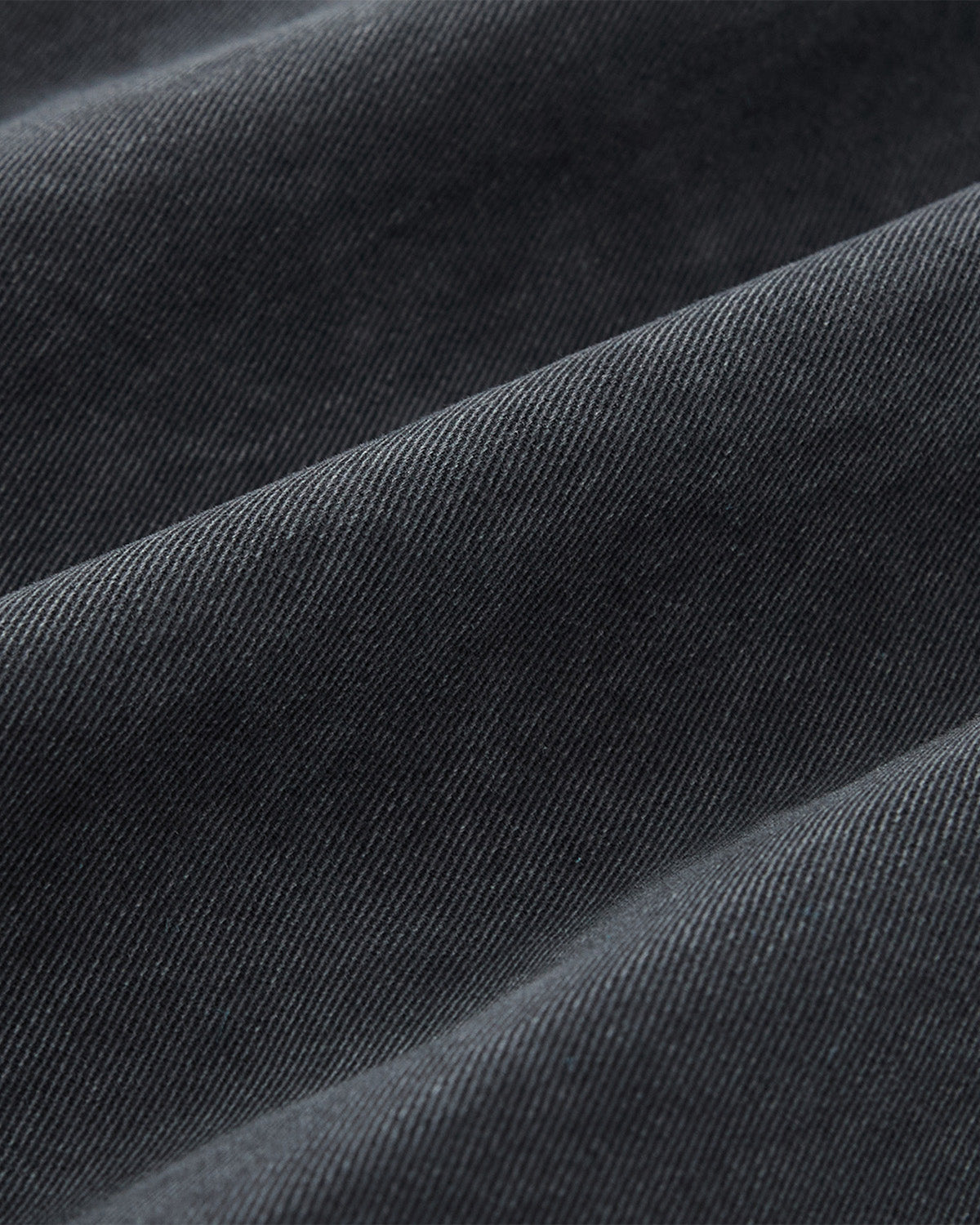 Close-up of dark grey fabric with a diagonal weave, showcasing the textured, three-dimensional look of Sundae School’s CHARCOAL HANBOK CHINO PANTS and their hanbok-inspired silhouette.