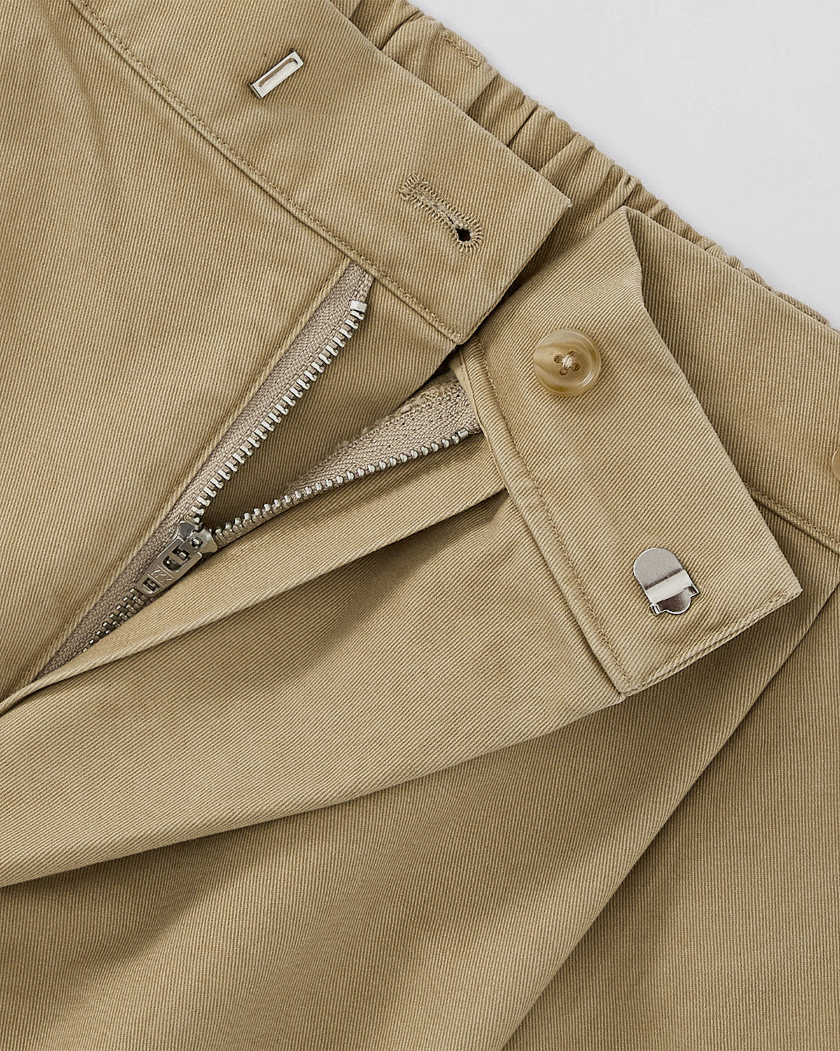 Close-up of OLIVE HANBOK CHINO PANTS by Sundae School, showing waistband with open zipper, button, and metal hook-and-bar closure. The fabric features a subtle diagonal weave and hanbok-inspired silhouette.