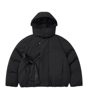 Introducing the BLACK IBUL DOWN PUFFER by Sundae School: an oversized black puffer jacket featuring a high collar, snap button closure, and a unique tied fabric belt detail on the left side of the waist. This style is designed with a detachable hood for versatile wear.