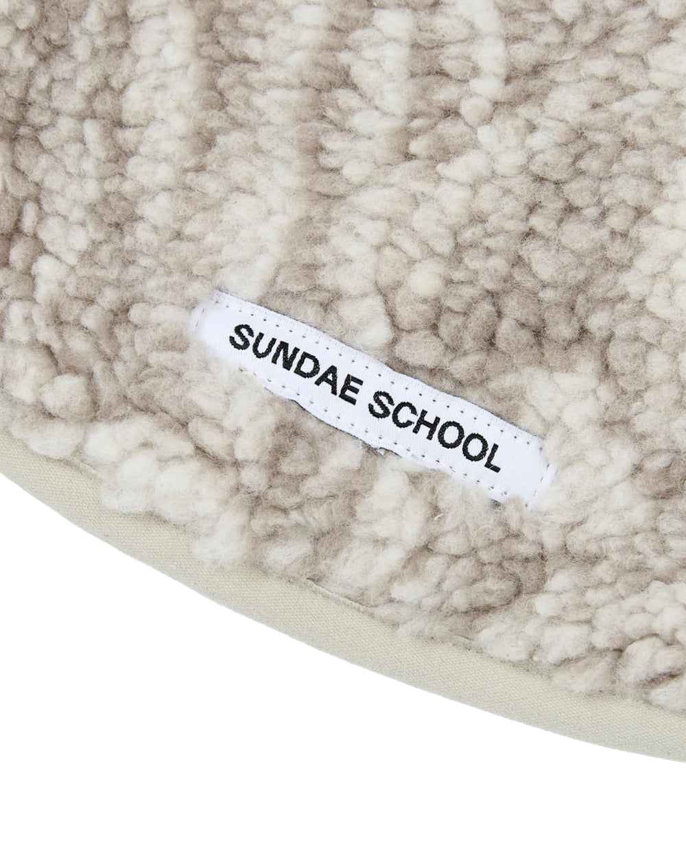 A close-up of the TAUPE IREZUMI DOGGIE FLEECE by Sundae School, featuring beige and white sherpa fleece fabric with a white label reading SUNDAE SCHOOL in black text—ideal for crafting custom jacquard dog fleeces or adjustable pet jackets.