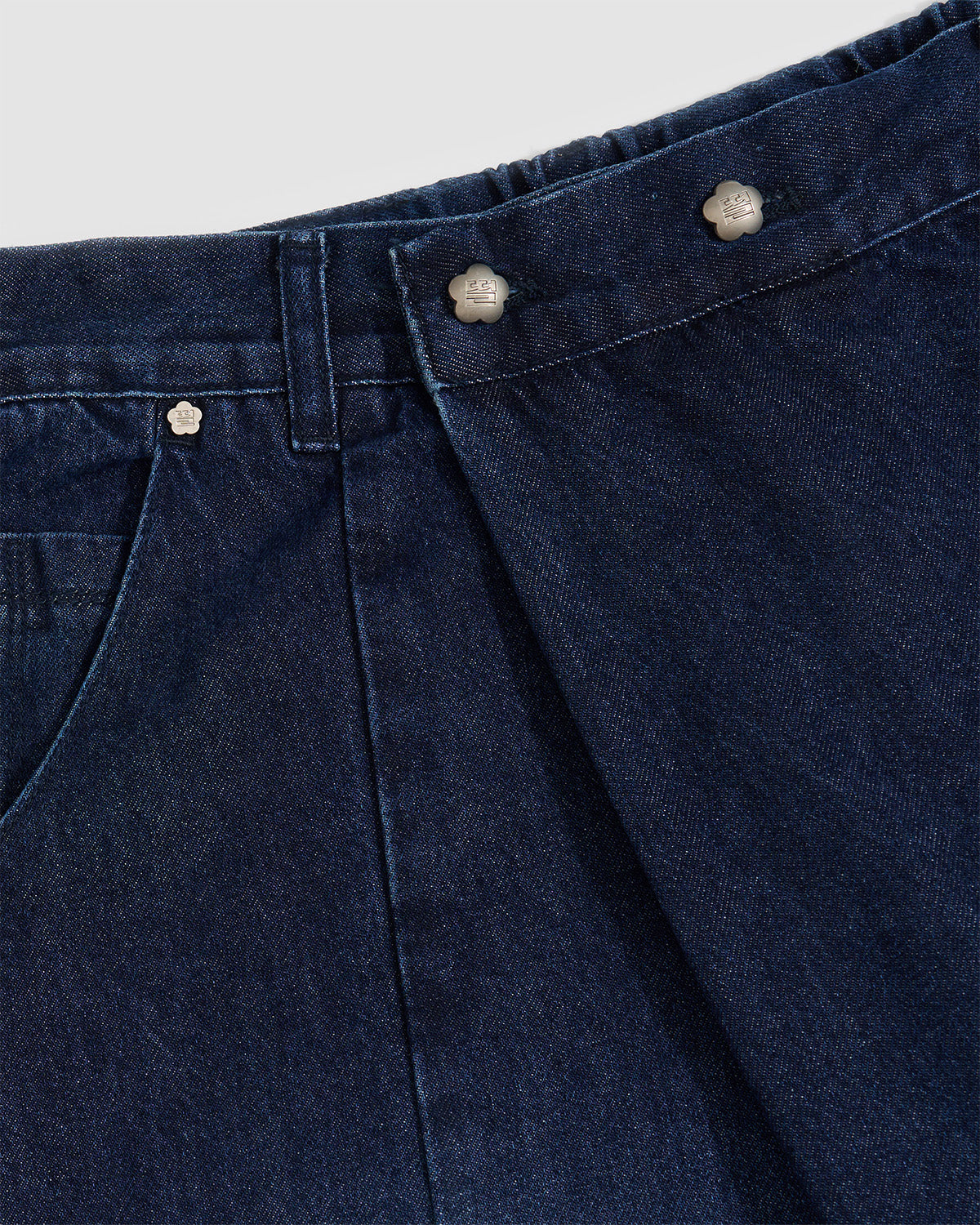 Close-up detail of indigo fade hanbok denim waistband showing silver flower-shaped snap buttons and asymmetric front closure design, highlighting custom hardware and button placement