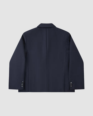 The Sundae School NAVY DOUBLE DUTY BLAZER, a navy wool blend with long sleeves, cuff buttons, and a subtle hanbok silhouette, is shown from the back against a plain light gray background.