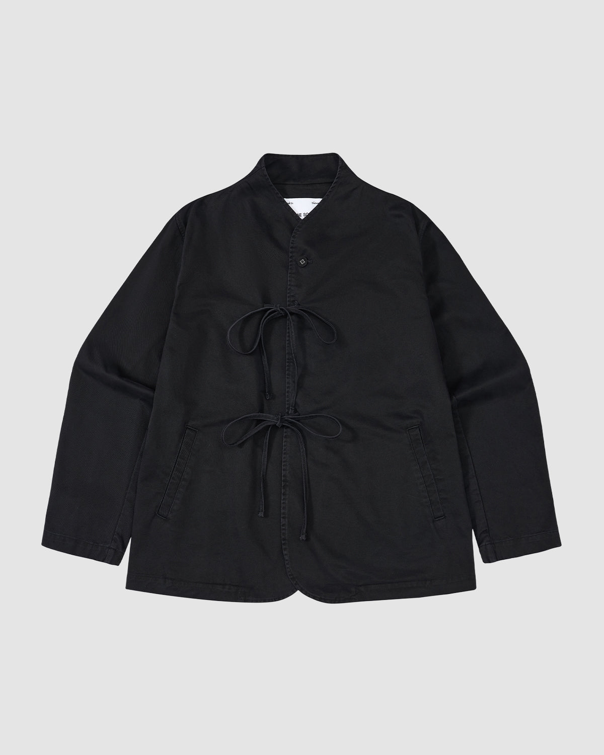 The BLACK JEOGORI TIE JACKET by Sundae School is a black, long-sleeve jacket with a monk collar, double goreum tie closures, and two front pockets, shown laid flat on a light gray background.