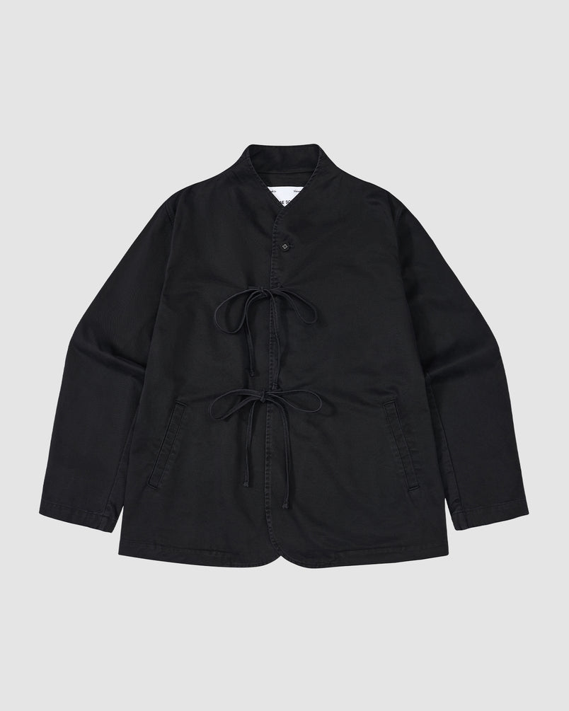 The BLACK JEOGORI TIE JACKET by Sundae School is a black, long-sleeve jacket with a monk collar, double goreum tie closures, and two front pockets, shown laid flat on a light gray background.