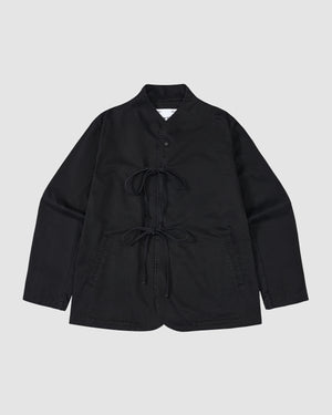 The BLACK JEOGORI TIE JACKET by Sundae School is a black, long-sleeve jacket with a monk collar, double goreum tie closures, and two front pockets, shown laid flat on a light gray background.