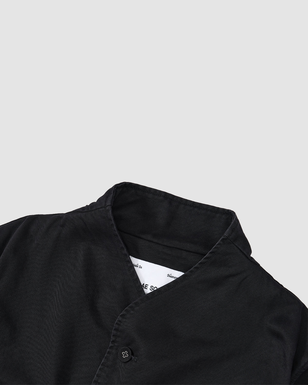 A cropped view of the BLACK JEOGORI TIE JACKET by Sundae School, featuring a monk collar and button-up front in a subtle Jeogori silhouette, set against a plain light gray background.