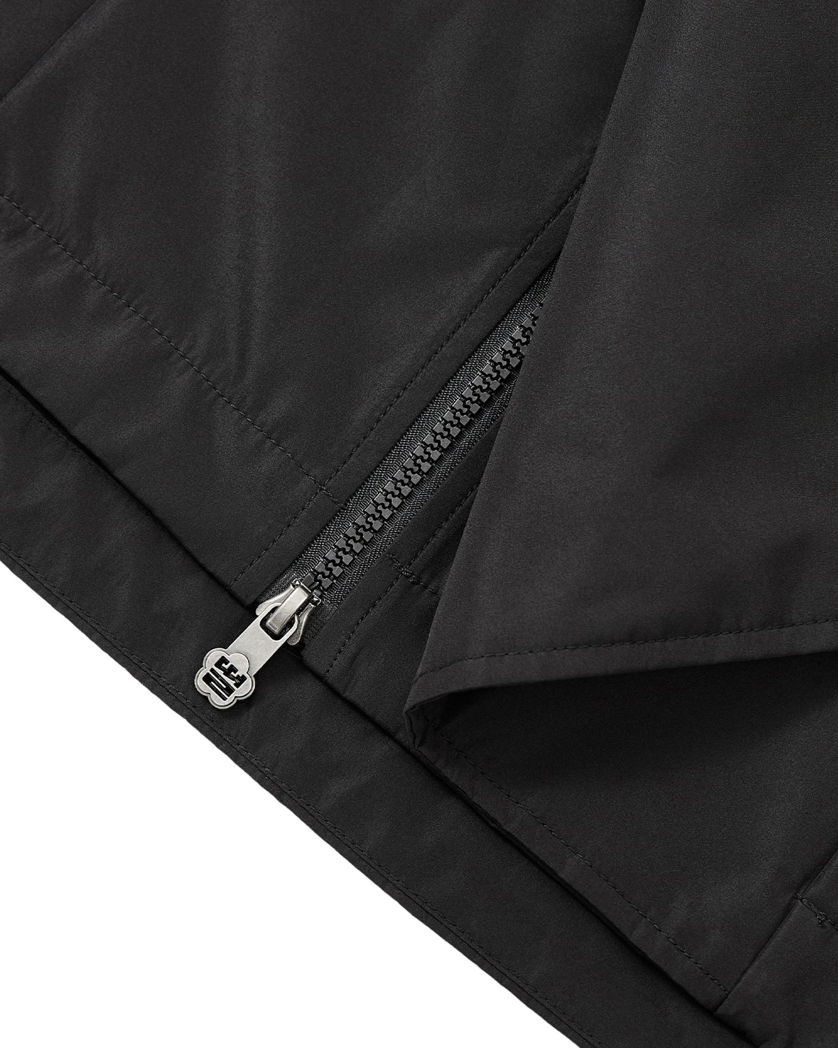 Close-up of the BLACK JEOGORI TIE SHELL JACKET by Sundae School, a black water-resistant outerwear piece featuring a partially unzipped silver zipper with a fabric flap overlapping one side. Inspired by the silhouette of a Korean jeogori jacket, this unisex technical gear combines modern utility with traditional design elements.