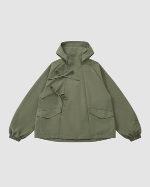 The MATCHA JEOGORI TIE SHELL JACKET by Sundae School features an olive green color, asymmetric front closure with three fabric bows, two front pockets, elastic cuffs, and a plain light gray background in a Korean-inspired style.