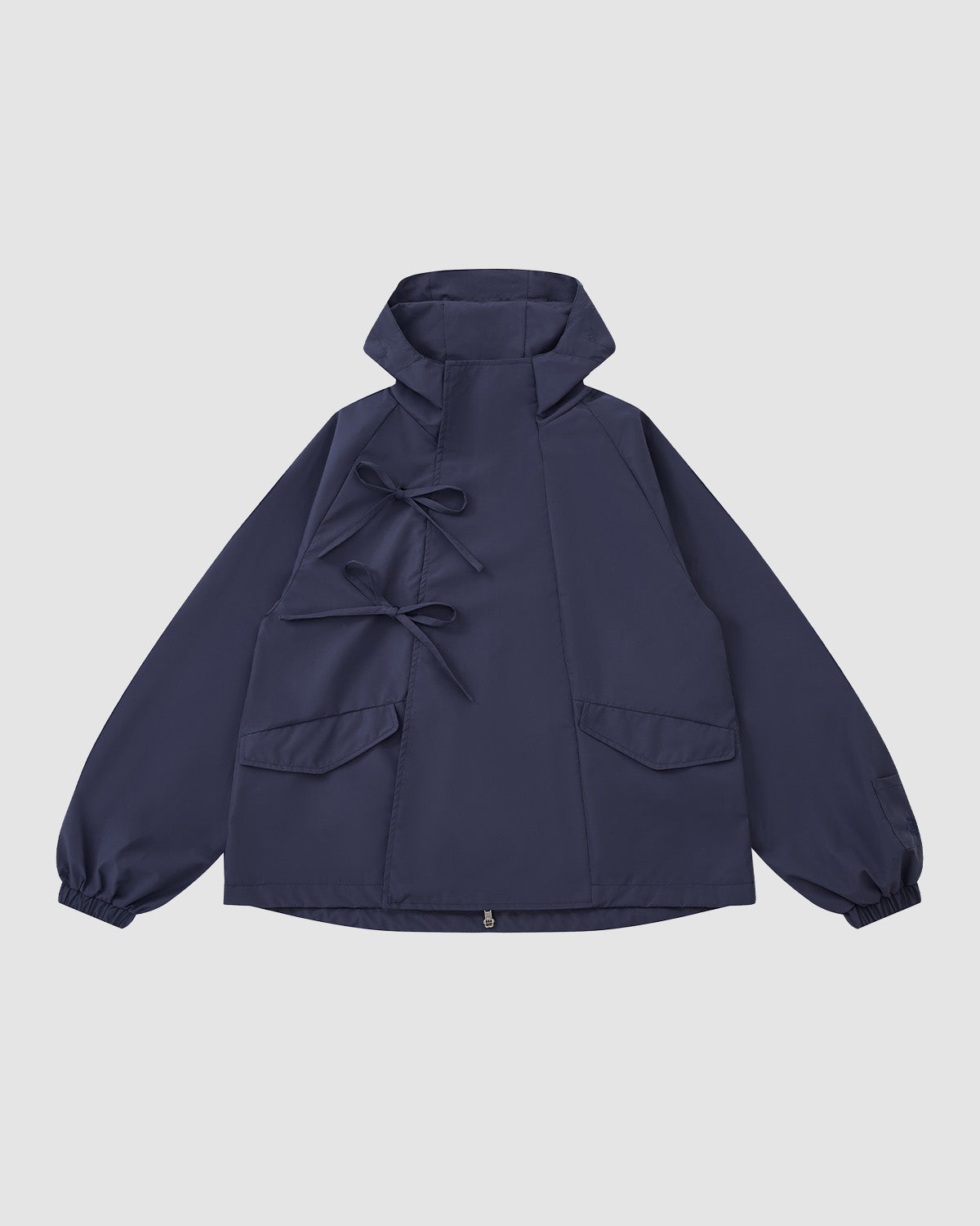 The Sundae School NAVY JEOGORI TIE SHELL JACKET features a water-resistant navy shell, two front pockets, elastic cuffs, and dual bow tie closures, shown against a plain light gray background.
