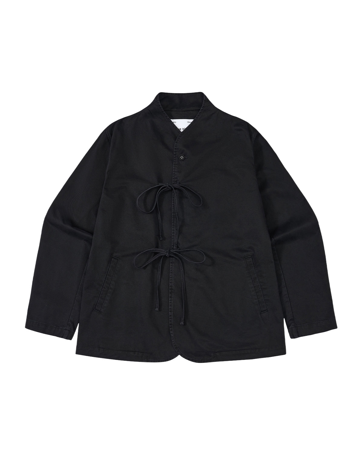 The BLACK JEOGORI TIE JACKET by Sundae School features a monk collar, jeogori-inspired design, two front pockets, and double goreum tie closures. Made from lightweight chino fabric, the jacket is displayed laid flat on a white background.
