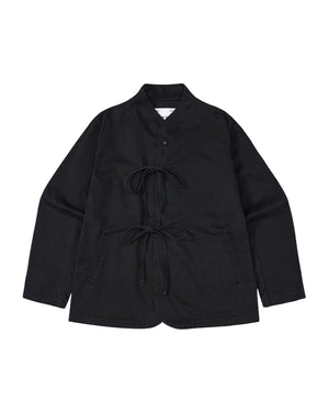 The BLACK JEOGORI TIE JACKET by Sundae School features a monk collar, jeogori-inspired design, two front pockets, and double goreum tie closures. Made from lightweight chino fabric, the jacket is displayed laid flat on a white background.