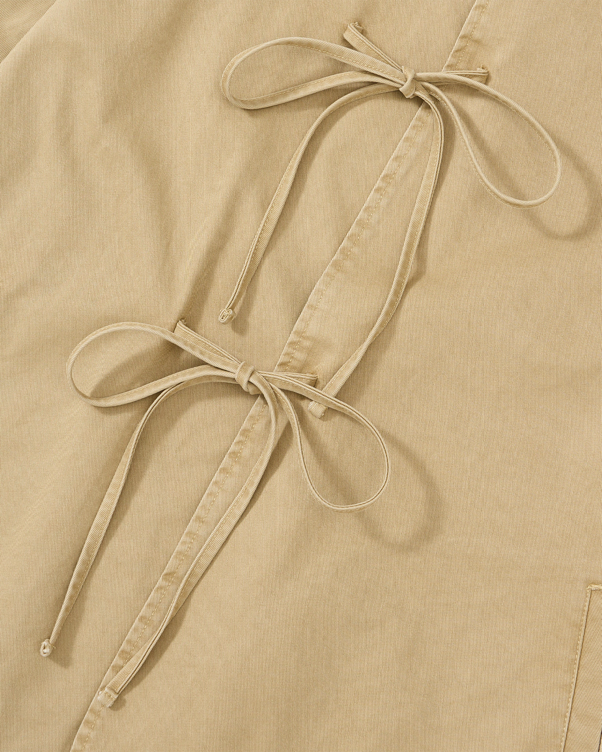 Close-up of the Sundae School TAN JEOGORI TIE JACKET, featuring beige fabric accented with two bows crafted from slender fabric strips and attached along a stitched seam—a nod to the traditional detailing found on summer suiting or the classic jeogori.