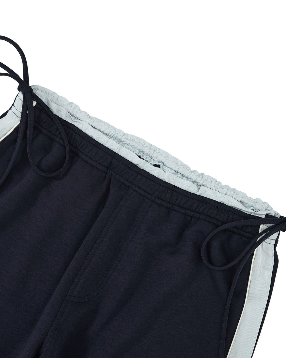 Close-up of Sundae School’s NAVY PALISADE PARK TRACK PANTS, featuring white side stripes and a drawstring waistband, designed as breathable stretch pants, laid flat on a white background.