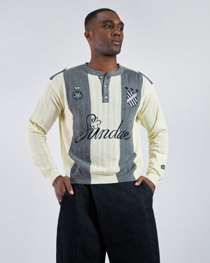Butter Yellow Charcoal Sundae Soccer Jersey Knit modeled on Black male model featuring vertical stripes, henley button placket, "Sundae" script embroidery across chest, numbered patches and crest details, styled with black wide-leg pants on light background, front view pose with hands in pockets.