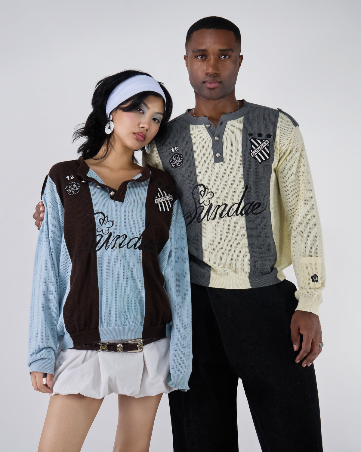 Three-quarter view of two models wearing coordinating Sundae Soccer Jersey Knits - female model in Baby Blue Brown Sundae Soccer Jersey Knit with white headband, brown belt, and white mini skirt, male model in Butter Yellow Charcoal colorway with black pants, showing complementary styling and design consistency.