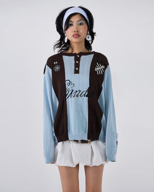 Baby Blue Brown Sundae Soccer Jersey Knit modeled on Asian female model wearing white headband and white earrings, featuring light blue and brown vertical stripes, henley button placket, "Sundae" script embroidery across chest, numbered patches and crest details, styled with white mini skirt and brown belt on light background, front view pose.