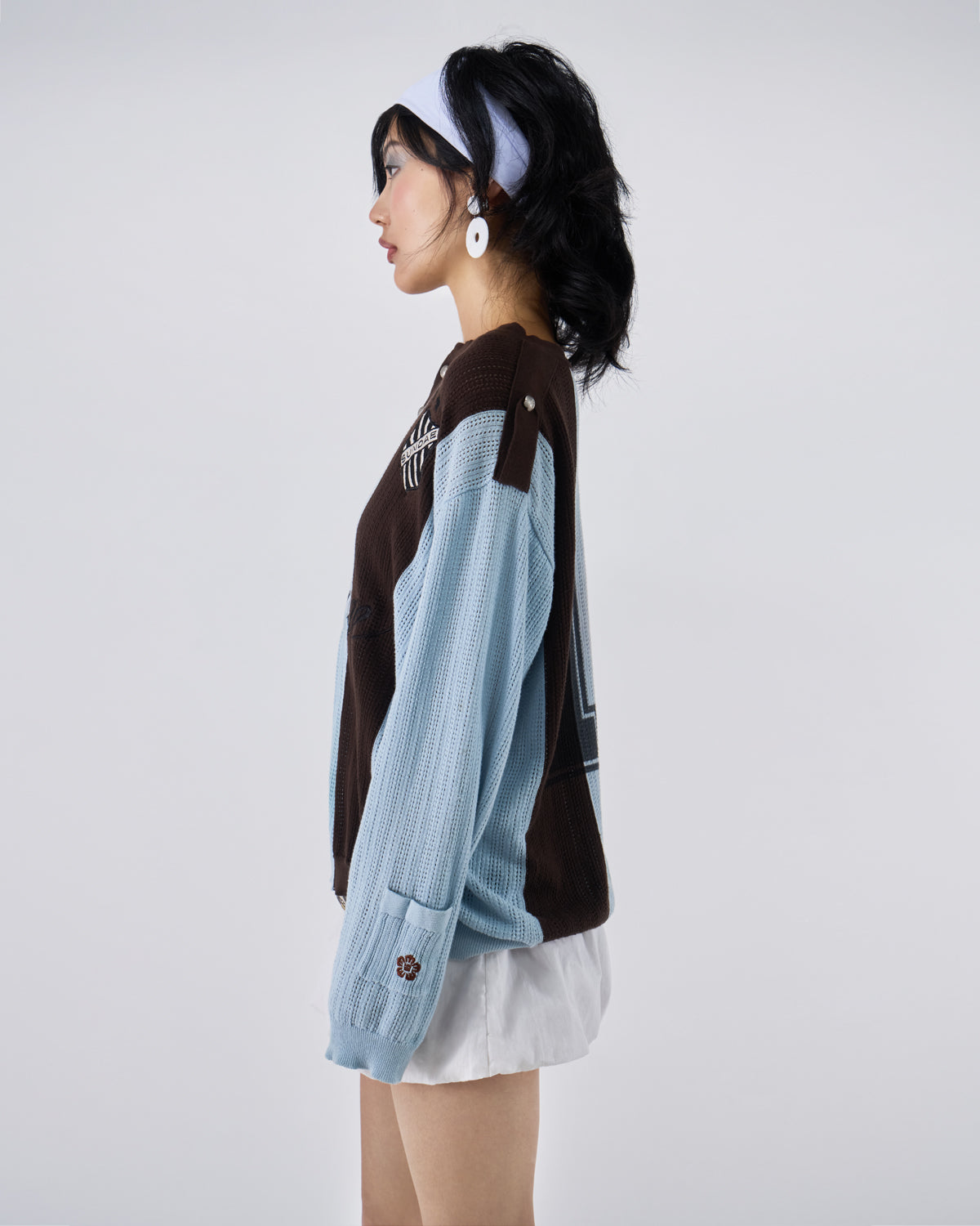 Side profile view of Baby Blue Brown Sundae Soccer Jersey Knit showing relaxed fit silhouette, vertical stripe pattern continuation, ribbed sleeve construction, and shield logo placement, styled with white mini skirt, photographed against light background.