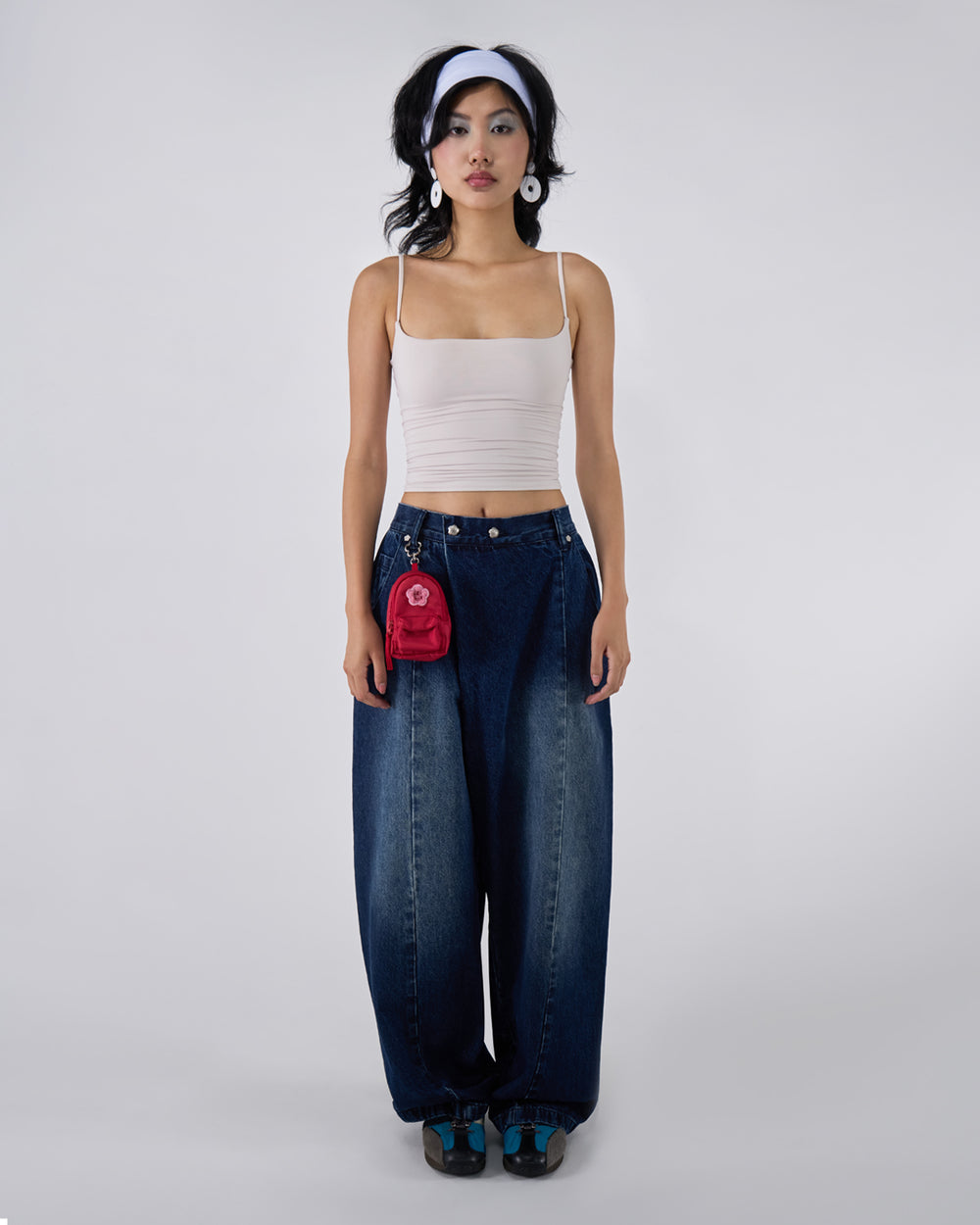 Indigo fade wide-leg hanbok denim pants modeled with white ruched bandeau crop top, white headband, and white disc earrings, red mini backpack accessory attached to waistband, full-length front view against white studio background