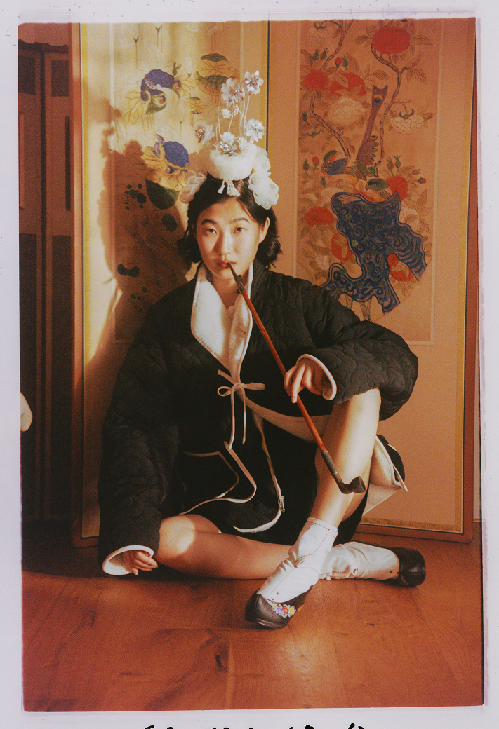 A model wearing Sundae School Black Ivory Reversible Flower Quilted Jeogori Fleece sitting  in a Korean traditional hanok room.