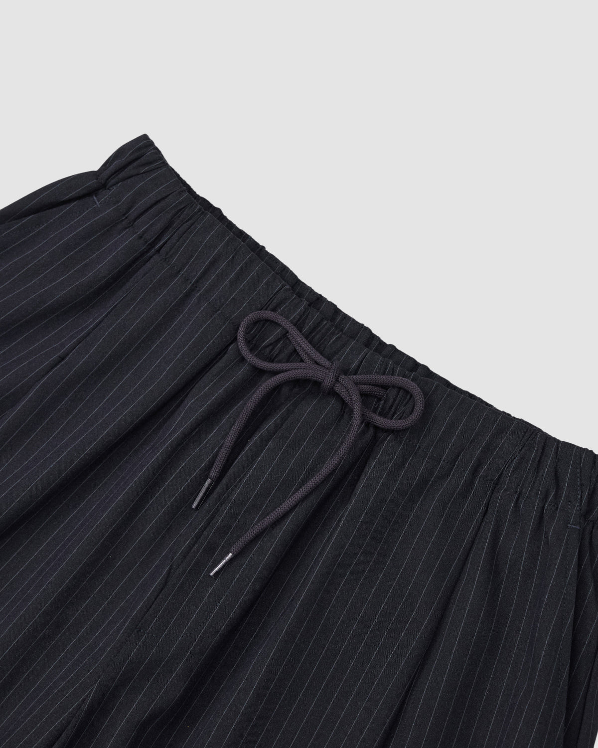 The KIKI DRAWSTRING SLACKS by Sundae School feature a relaxed barrel leg, an elastic drawstring waist tied in a bow, and thin white pinstripes, displayed against a plain light gray background.