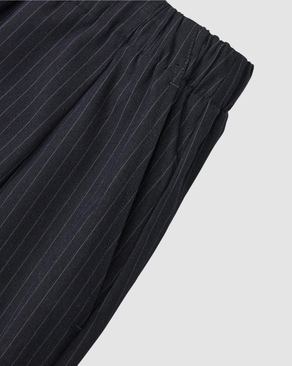 Close-up of Sundae School's KIKI DRAWSTRING SLACKS in black pinstripes, showing the elastic waistband, gathered pleats, and relaxed barrel leg silhouette.