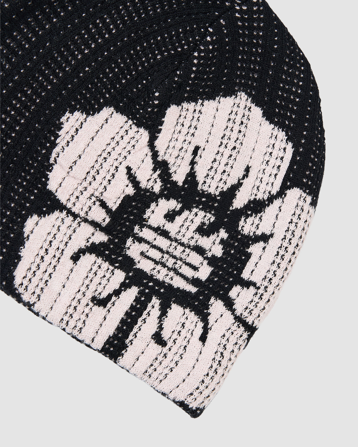 A close-up of the BLACK DDUL KNIT BEANIE from Sundae School in black, featuring a bold, abstract white flower design. The breathable knit and striking contrast make it perfect for a minimalist spring look.