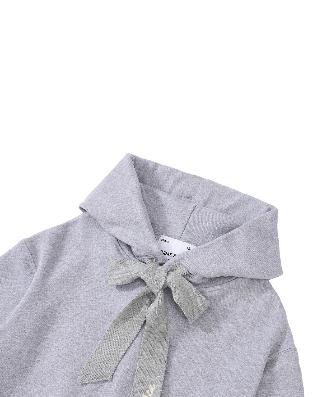 The HEATHER GREY KNIT TIE HOODIE by Sundae School features a relaxed unisex fit and is crafted from soft, brushed cotton for extra comfort and warmth. It showcases a light heather gray color, a wide collar, and includes a matching fabric tie at the neckline. Displayed against a white background.