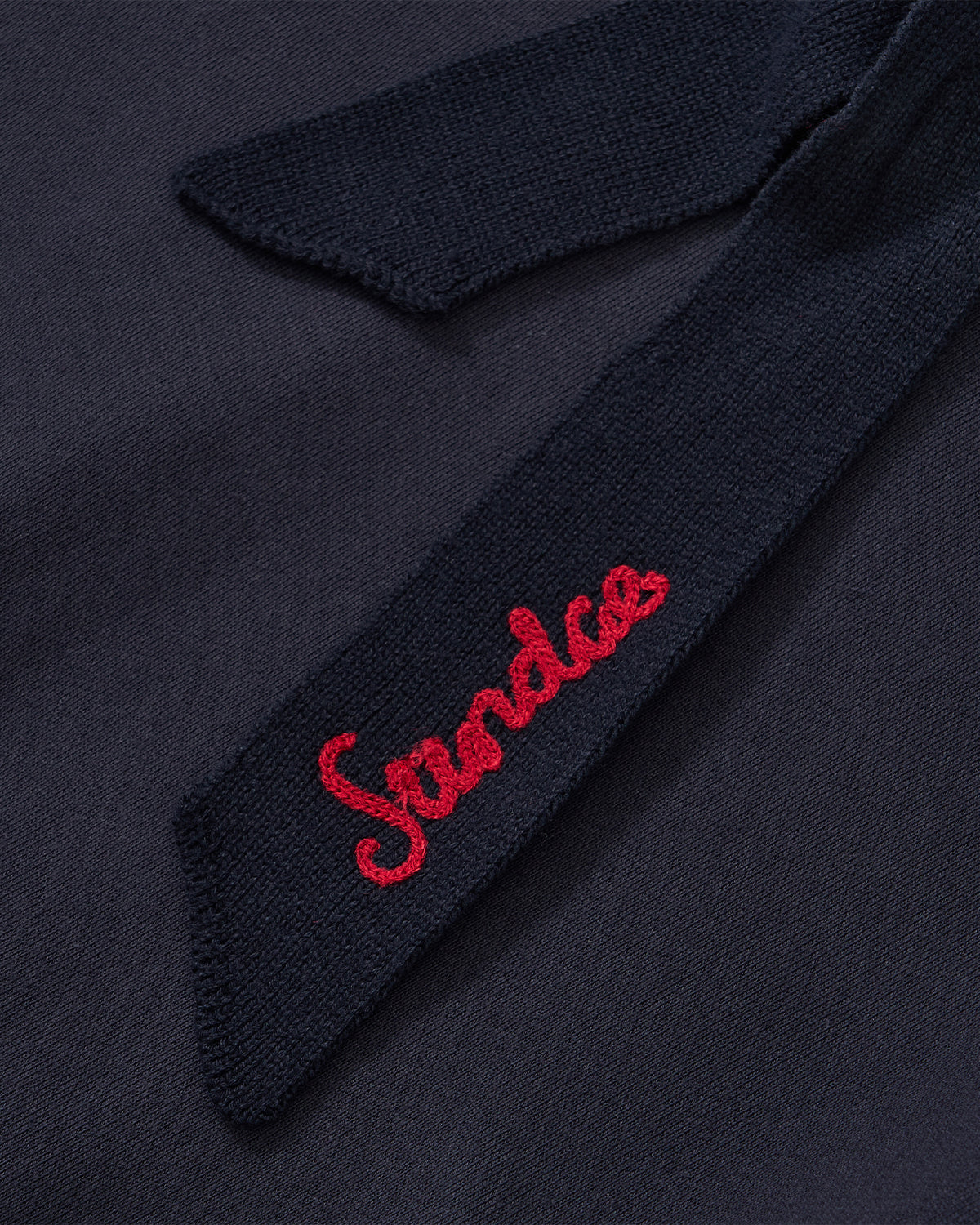 A close-up of the Sundae School NAVY KNIT TIE HOODIE shows its dark blue fabric tie, 