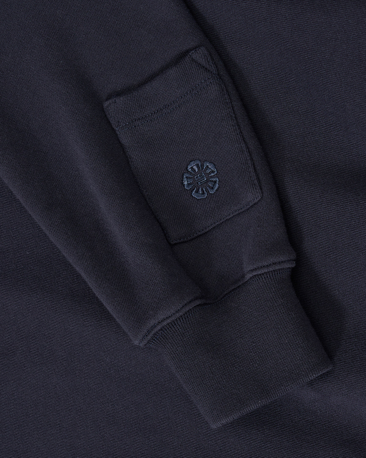 A close-up of the Sundae School NAVY KNIT TIE HOODIE sleeve shows a small rectangular pocket with an embroidered flower near the ribbed cuff.