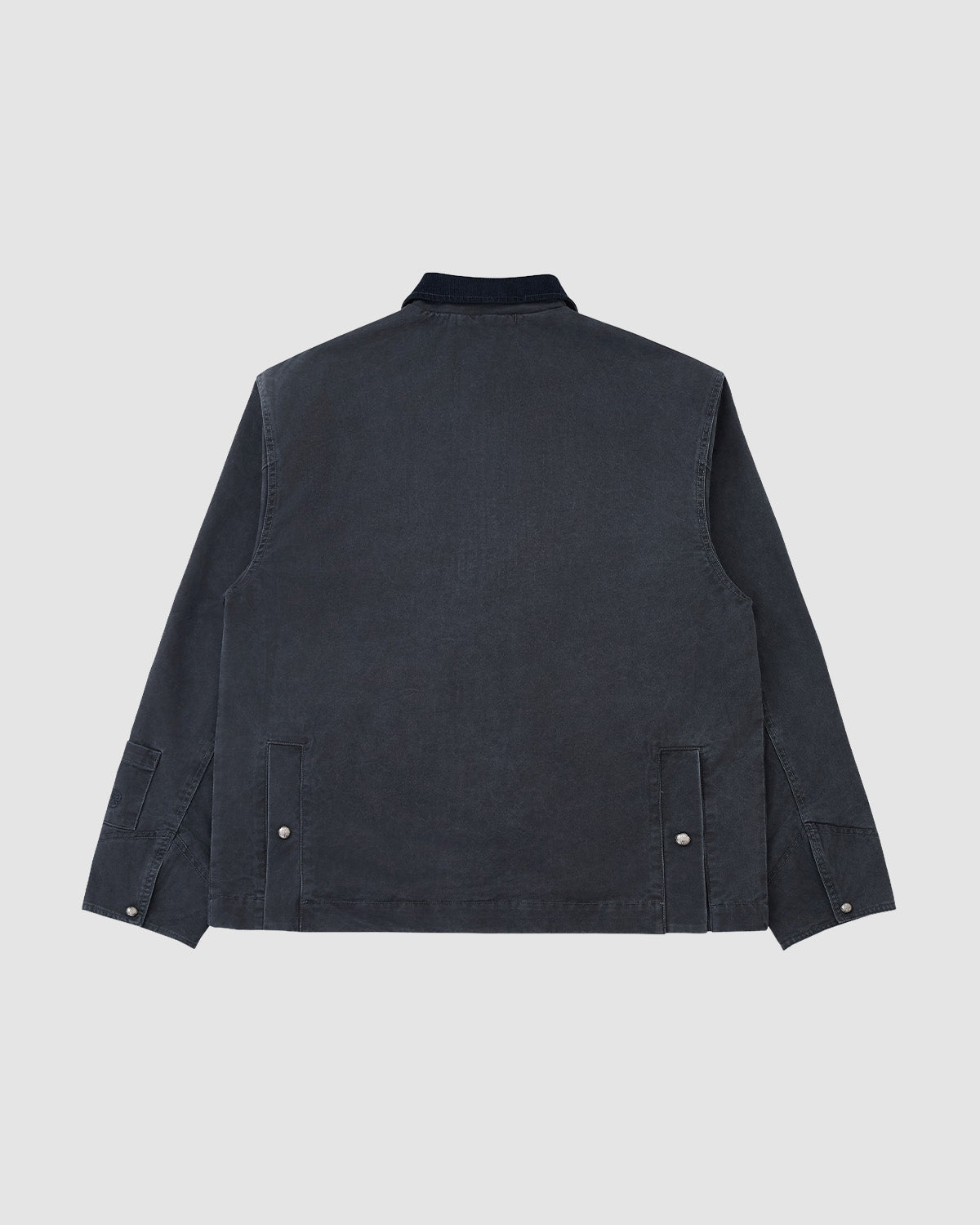 The Sundae School CHARCOAL KNOT BARN JACKET is a long-sleeved, dark blue jacket seen from the back, with a straight collar, buttoned cuffs, and two adjustable side tabs. Its simple design is inspired by Joseon military heritage workwear. No visible logos or patterns.