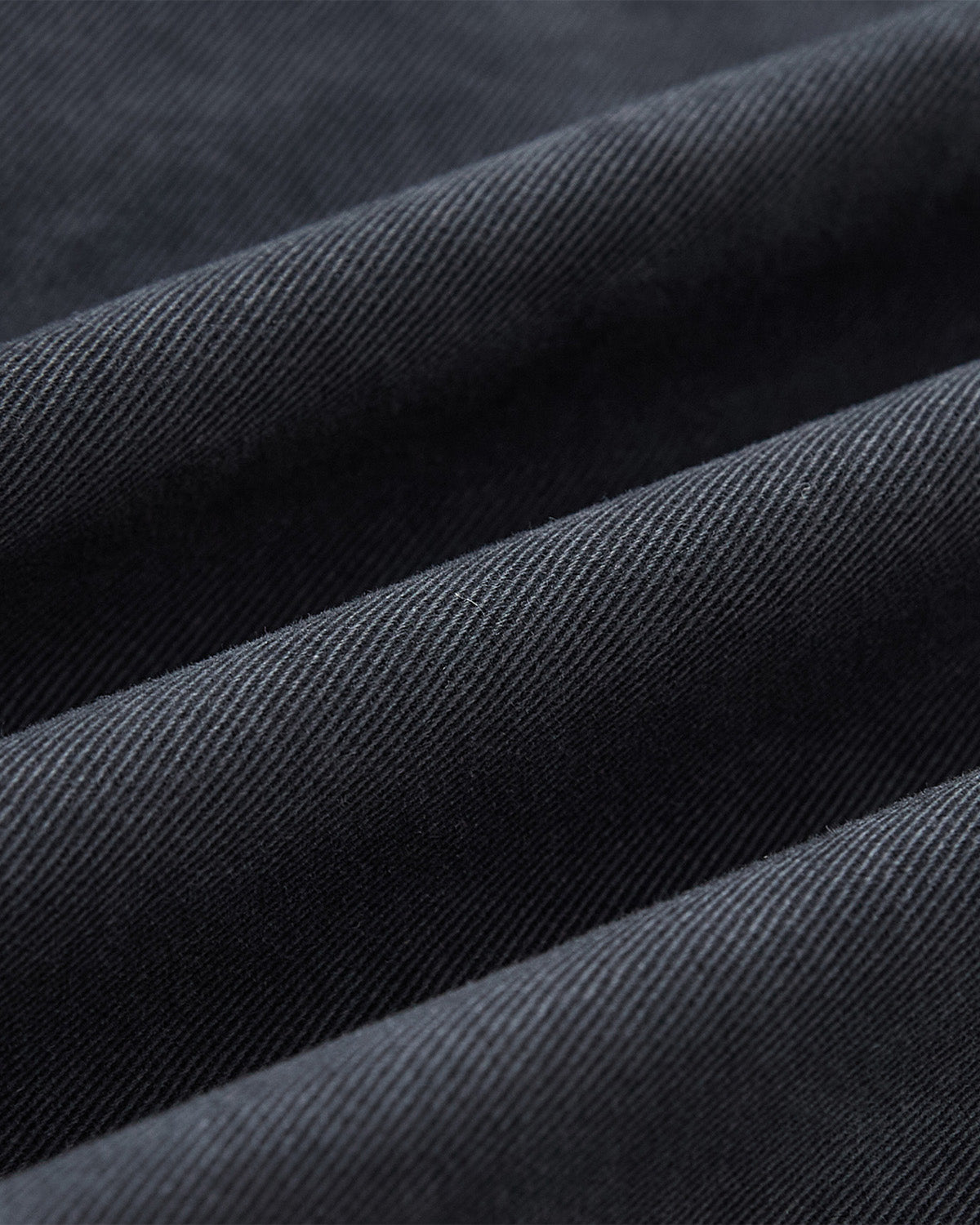 Close-up of folded enzyme-washed waxed chino on the Sundae School CHARCOAL KNOT BARN JACKET, highlighting its fine diagonal weave and soft shadows for a heritage workwear-inspired texture.