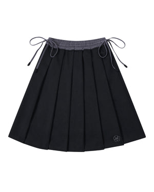 Introducing the BLACK KONA MIDI SKIRT by Sundae School—a black pleated skirt featuring a gray waistband and adjustable side ties. A small embroidered flower accent decorates one corner. The skirt is displayed laid flat against a white background.
